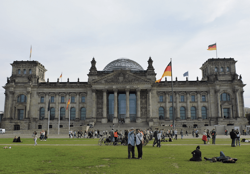 Der Bundestag in Berlin, auf dem Rasen liegen zahlreiche Menschen und genießen die Sonne.