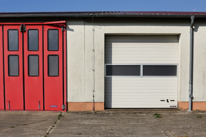 Ein rotes Garagentor auf einem Hinterhof ist zu sehen. Ob eine Garage zum Sondereigentum oder zum Gemeinschaftseigentum gehört, dazu gibt es immer wieder Fragen. Wir beantworten sie in diesem Kapitel.
