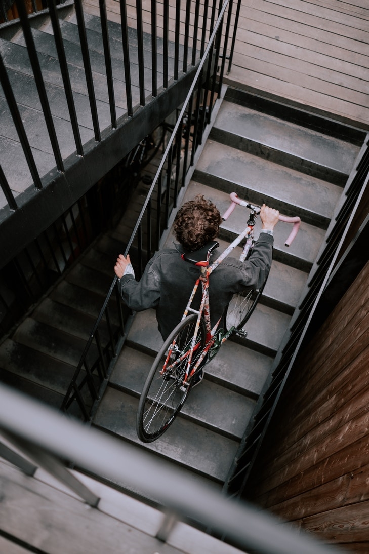 Ein junger Mann trägt ein Rennrad einen Hausflur hinauf. Abgestellte Gegenstände im Treppenhaus sorgen immer wieder für Zwist in WEGs.