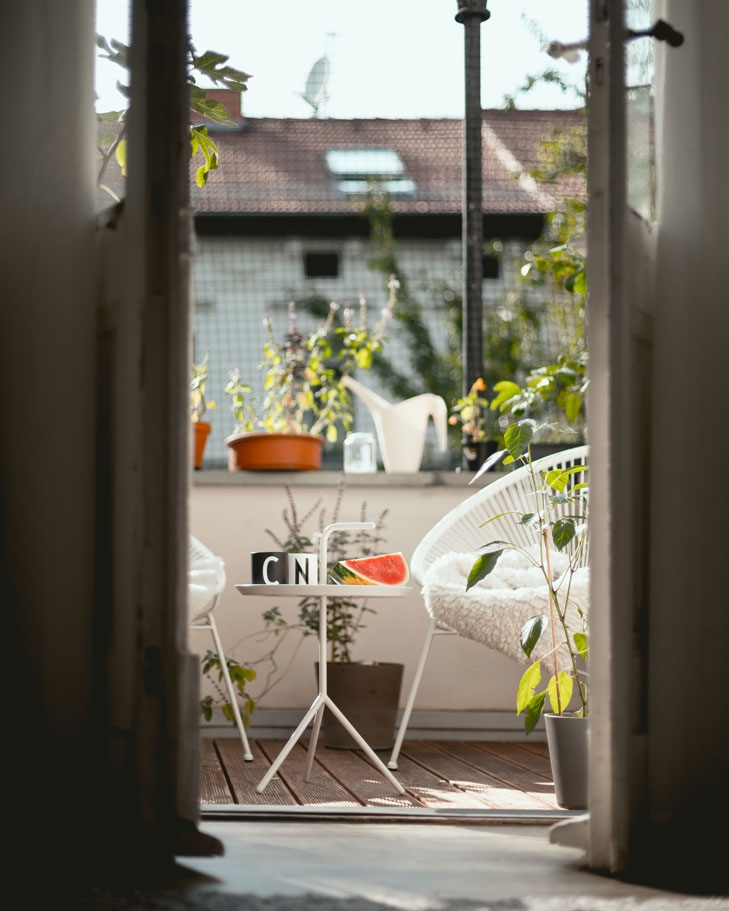 Ein geöffnetes Fenster geht auf einen sonnigen Balkon. Im WEG hat der Balkon eine Sonderrolle, denn er ist sowohl Sondereigentum als auch Gemeinschaftseigentum.
