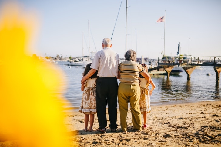 Großeltern stehen mit ihren Enkelinnen an einem Strand und schauen aufs Wasser.