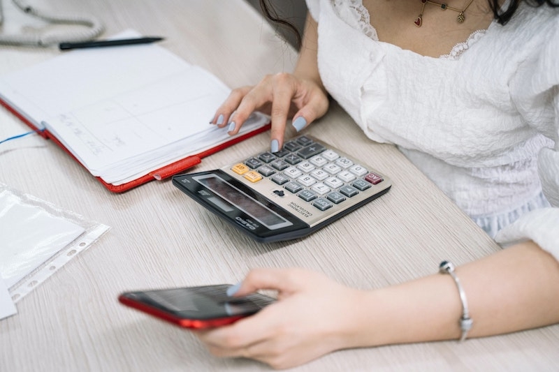 Eine Frau hält ein Smartphone in der Hand und nutzt einen Kalkulator, um Kosten von ihrer Immobilie abzuschreiben.