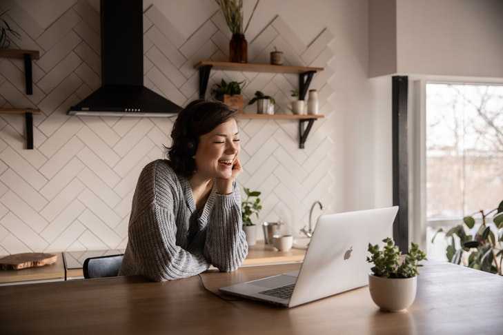 Eine junge Frau sitzt in einer Wohnung am Küchentisch vor einem aufgeklappten Laptop. Mittlerweile kann man an Eigentümerversammlungen auch digital teilnehmen. Dafür gibt es jedoch einige Voraussetzungen, die wir in diesem Artikel erläutern.