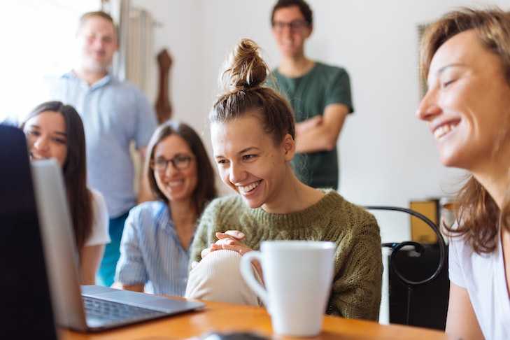 Auf dem Bild ist eine Gruppe junger lachender Menschen vor einem Laptop zu sehen.