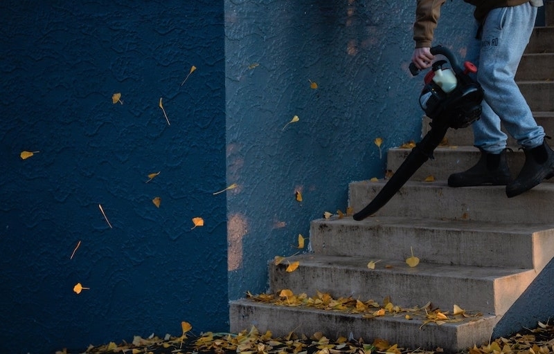 Ein Mann steht auf einer Treppe und hält einen Laubbläser. Jetzt verraten wir Ihnen, was zu umlagefähigen und nicht umlagefähigen Nebenkosten gehört