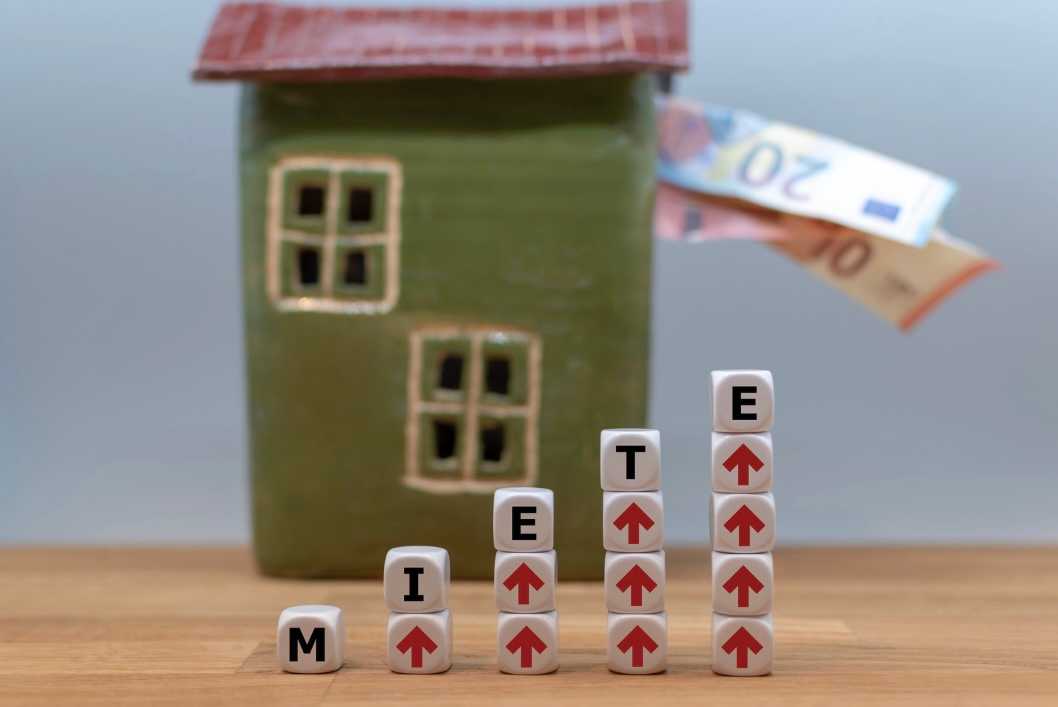 Auf einem Tisch steht ein grünes Häuschen aus Ton, aus dem Fenster hängen Euroscheine, davor steht das Wort Miete.