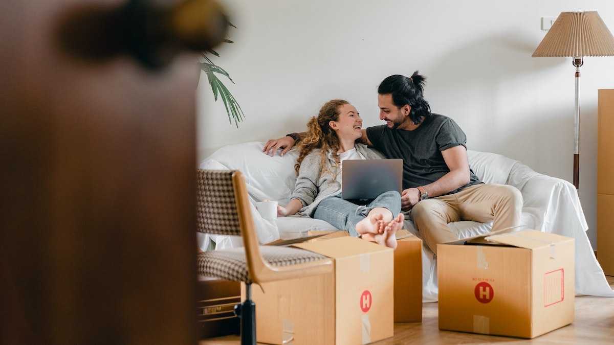 Ein junges Paar sitzt auf der Couch in ihrer neuen Eigetumswohnung und lacht