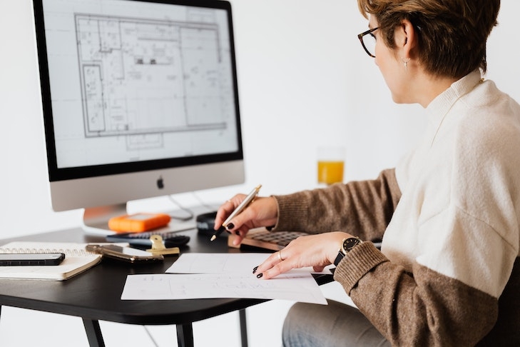 Eine Frau sitzt an einem Schreibtisch, auf dem Bildschirm ist der Grundriss einer Immobilie zu sehen