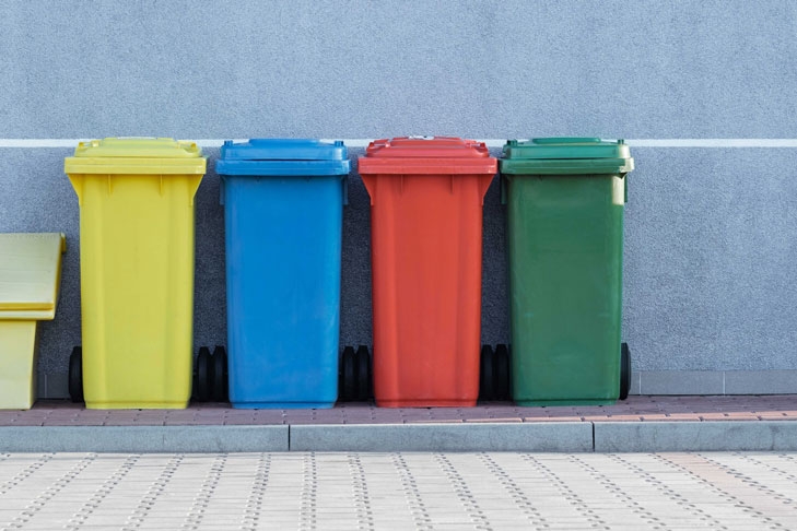 Vier bunte Mülltonnen stehen an einer Straße. Das Thema Müll sorgt in Wohnungseigentümergemeinschaften immer wieder für Streit. Eine gut formulierte Hausordnung schafft Abhilfe.