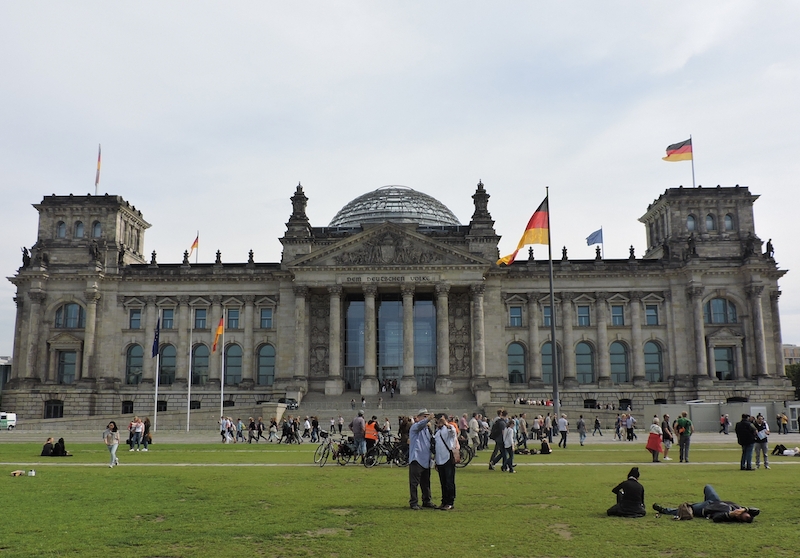 Der Bundestag in Berlin, auf dem Rasen liegen zahlreiche Menschen und genießen die Sonne.