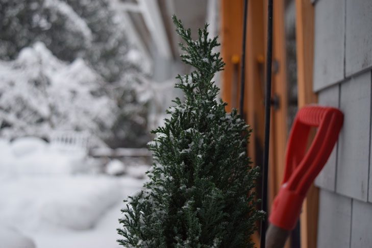 Eine Schneeschippe steht angelehnt an eine Hauswand. Pflichten in einem Mehrfamilienhaus wie der Winterdienst können nicht einem einzigen Eigentümer auferlegt werden, sondern müssen fair zwischen den Eigentümern aufgeteilt sein.