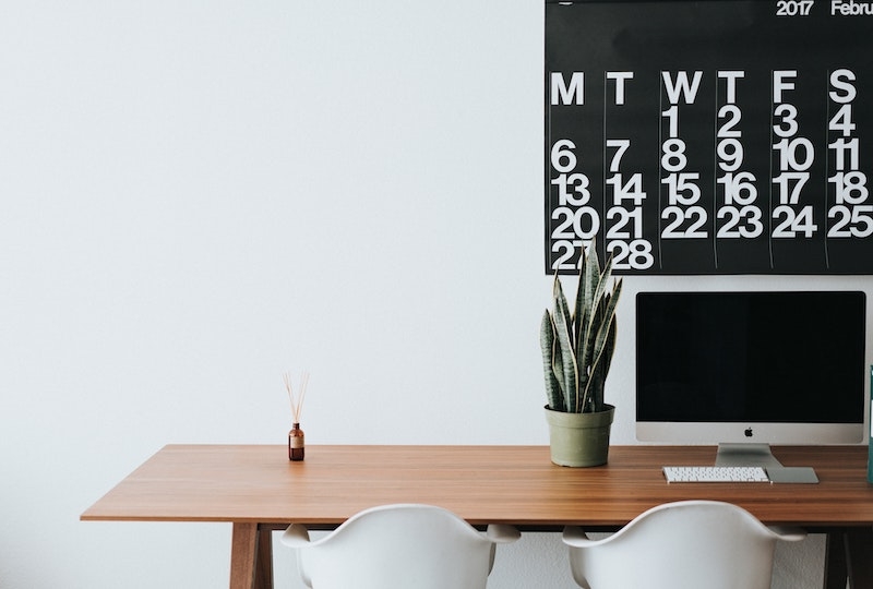 Ein modernes Arbeitszimmer mit einem Kalender an der Wand ist zu sehen. Jetzt erfahren Sie, welche Frist bei der Einberufung einer außerordentlichen Eigentümerversammlung zu bachten ist.