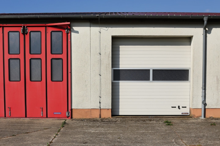 Ein rotes Garagentor auf einem Hinterhof ist zu sehen. Ob eine Garage zum Sondereigentum oder zum Gemeinschaftseigentum gehört, dazu gibt es immer wieder Fragen. Wir beantworten sie in diesem Kapitel.